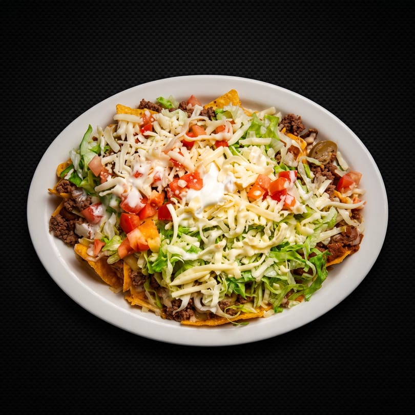 Plate of nachos topped with ground beef, lettuce, tomatoes, cheese, and sour cream.