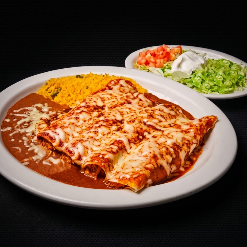 Cheesy enchiladas with rice, refried beans, and a side salad with lettuce, tomato, and sour cream.